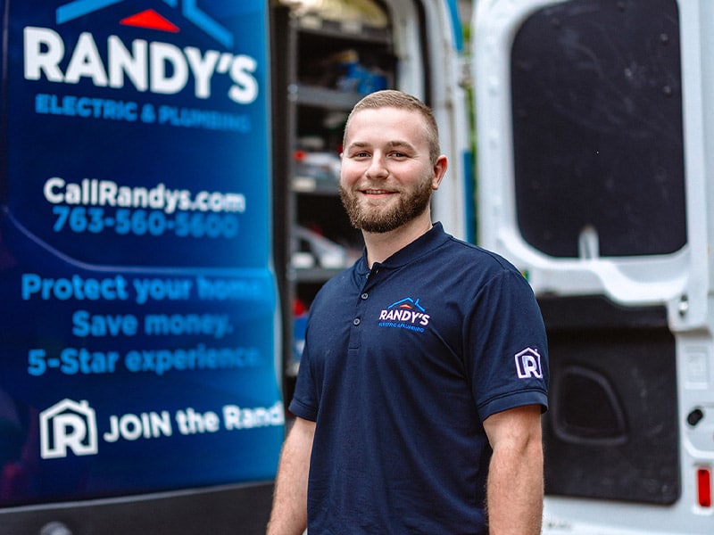 A man in a Randy's Electric & Plumbing shirt stands by a service van.